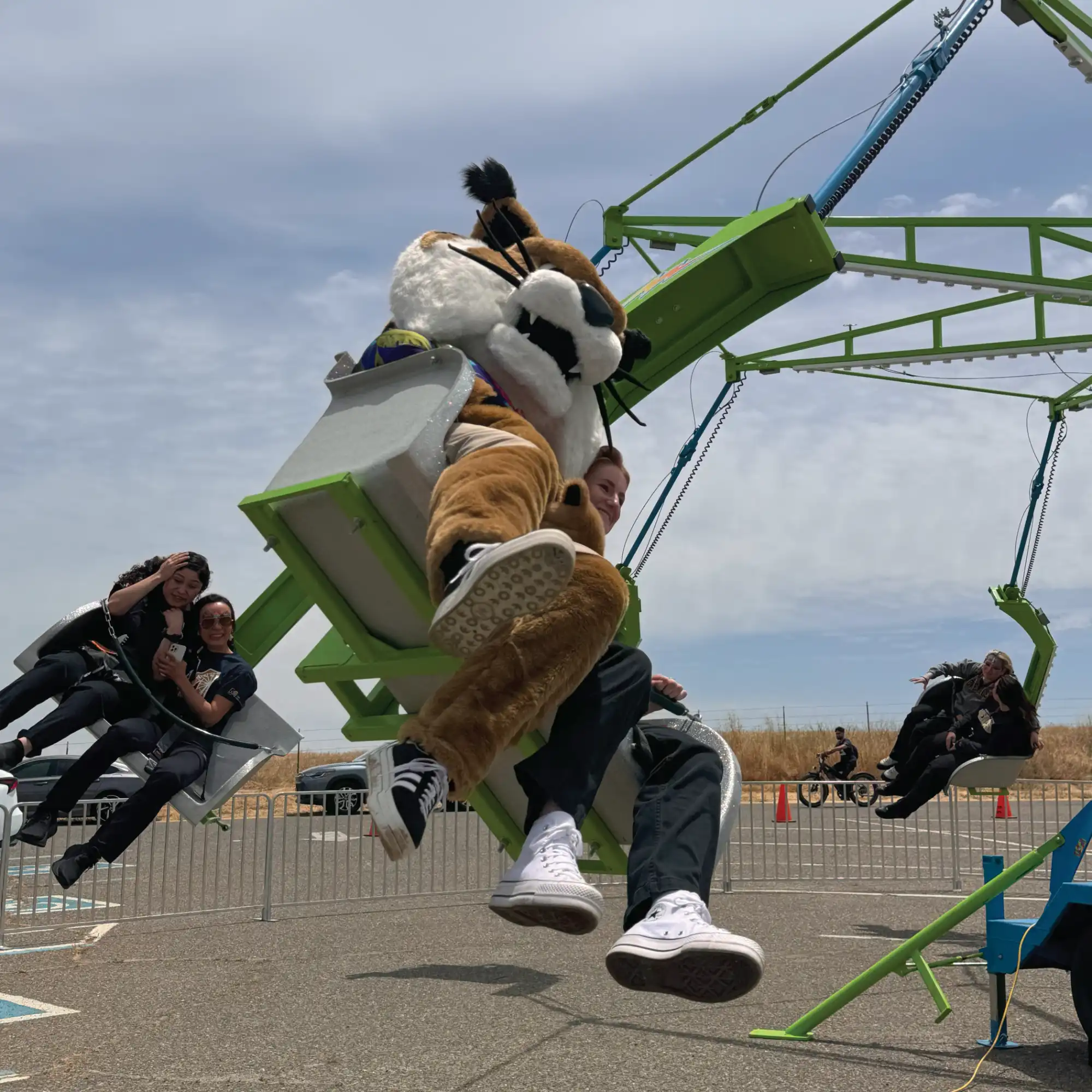 UC Merced Mascot, Rufus Bobcat, and staff riding a carnival ride at Lake Yosemite.